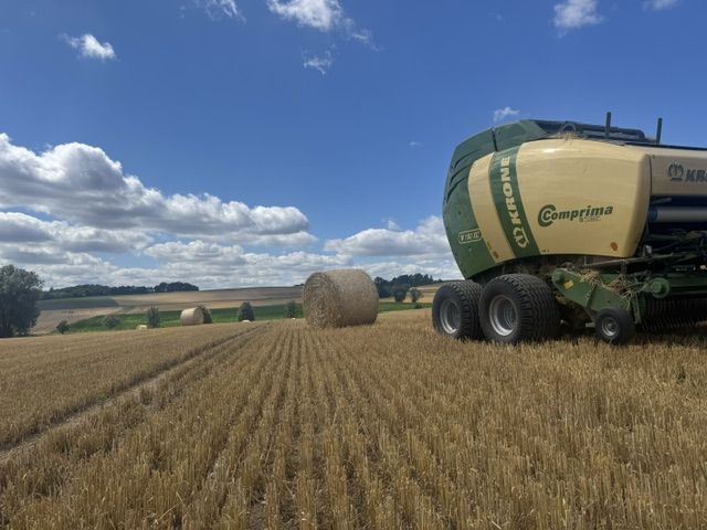 KRONE Comprima Rundballenpresse auf dem Stoppelfeld, im Hintergrund fertige Rundballen