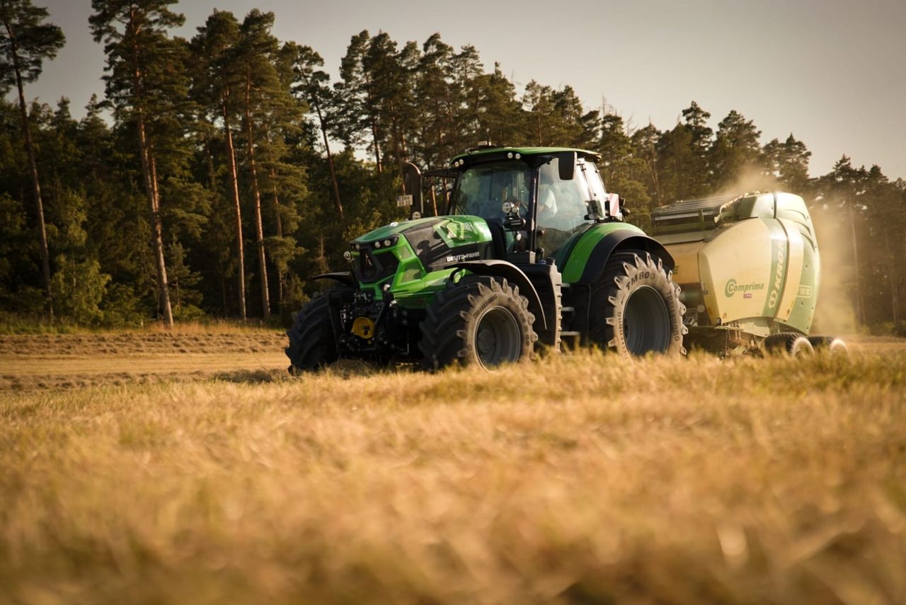 Deutz-Fahr Traktor mit KRONE Rundballenpresse im Abendlicht auf dem Getreidefeld
