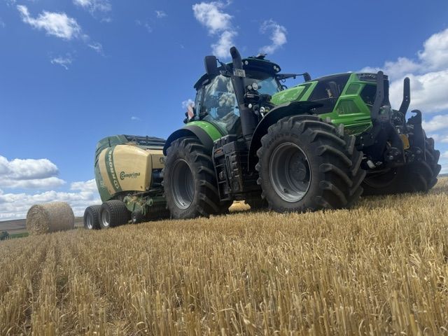 Traktor mit Rundballenpresse bei der Arbeit auf dem abgeernteten Feld